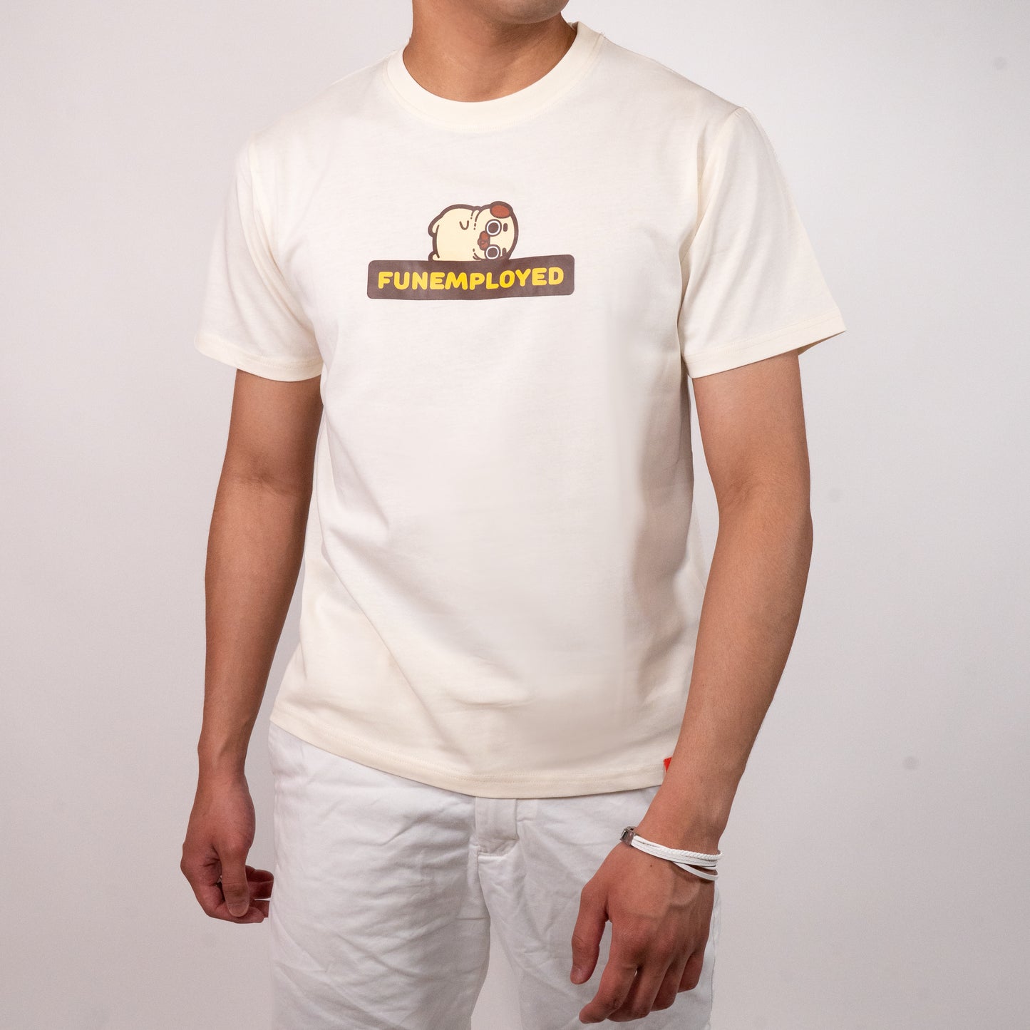 Person wearing a cream-coloured t-shirt with a graphic of Puglie laying down on the bolded all-caps yellow text outlined in black that says 'FUNEMPLOYED'. The graphic is in the center of the chest of the t-shirt.