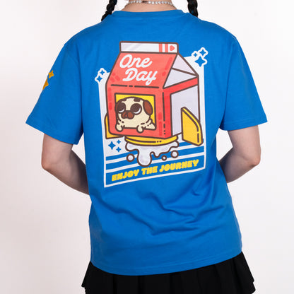 A person facing away from the camera wearing a blue t-shirt with a graphic of a red, white, and yellow rocket ship shaped like a milk carton with a tan-colored pug peeking out of window. The rocket appears to be blasting milk out the bottom, and the graphic is surrounded by a geometric white diagonal rectangle with cut-out lines and sparkle emoji. The graphic is in the centre of the back of the t-shirt. A small yellow design is visible on the shoulder. The model is wearing a black skirt.