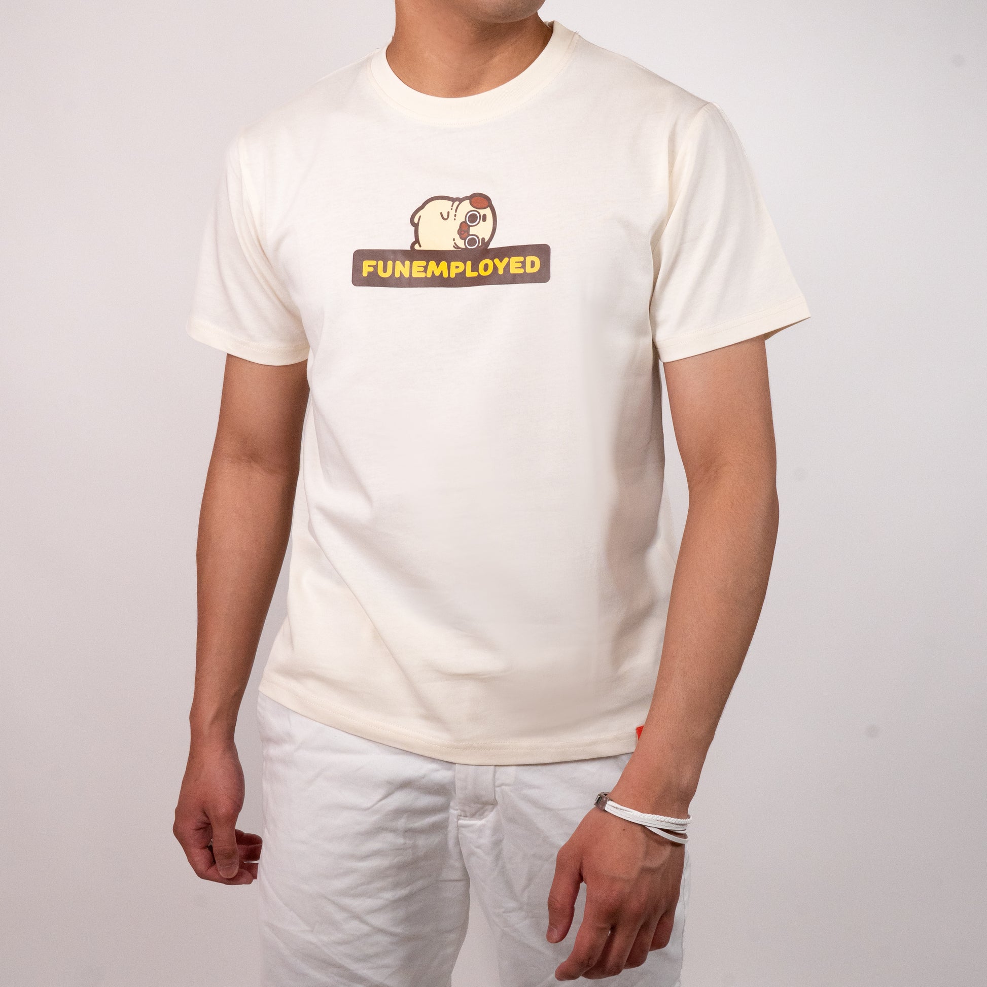 Person wearing a cream-coloured t-shirt with a graphic of Puglie laying down on the bolded all-caps yellow text outlined in black that says 'FUNEMPLOYED'. The graphic is in the center of the chest of the t-shirt.