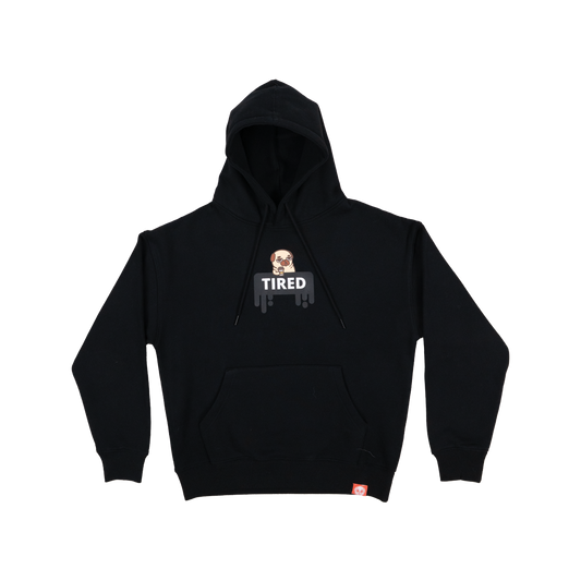 A black long-sleeved hoodie with a graphic of a tired-looking pug holding a to-go coffee cup above a black dripping rectangle with the white text "TIRED". The graphic is in the centre of the chest of the t-shirt. There is a small red tag on the bottom hem of the hoodie. 