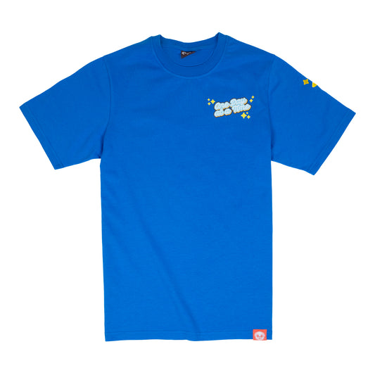 A blue t-shirt with a graphic of light blue and white cursive text saying 'One Day at a Time". The text is surrounded by yellow sparkle emoji. The graphic is in the top-left of the chest of the t-shirt. A small yellow sparkle design is visible on the shoulder. A small red tag with a Puglie face on the bottom hem of the shirt. 
