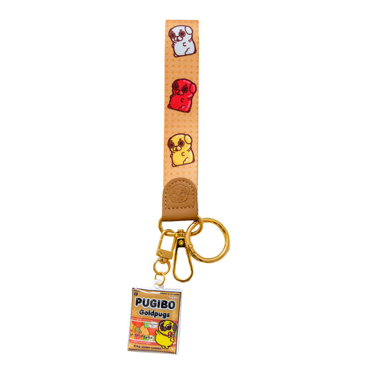 Keychain with a wrist strap featuring a design of candy-colored pugs (red, yellow, white) with a leather-looking clasp embossed with a pug face. The leather-looking clasp is stitched to the wristlet and attached to a gold oval hoop, which has a gold jump ring, a gold lobster clasp, and a gold hook clasp attached with a cute charm featuring Puglie-themed bag of candies. They are designed in the style of "Haribo" and called "PUGIBO GOLDPUGS".