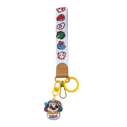 Keychain with a wrist strap featuring a design of many food items and one pug butt, with a leather-looking clasp embossed with a pug face. The leather-looking clasp is stitched to the wristlet and attached to a gold oval hoop, which has a yellow jump ring, a lobster clasp, and a hook clasp attached with a cute charm featuring Puglie in a bag with a bunch of food items surrounding him. The bag says "PUGLIE MART ❤️".